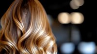 Luxurious wavy blonde and caramel balayage hair with soft highlights on dark background. Professional hairstyling showcasing modern coloring technique and healthy shine.