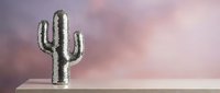 Silver metallic cactus sculpture on wooden shelf against soft pink purple gradient background for modern home decor and interior design concepts.