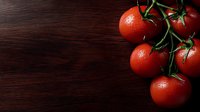 Fresh ripe red tomatoes on vine with water drops against dark wooden background, natural organic produce for healthy cooking and food photography.
