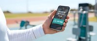 Hand holding smartphone with premium workout plan app screen at outdoor gym, fitness technology concept for sports and health marketing.