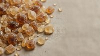 Brown and golden sugar crystals scattered on neutral beige surface, suitable for food, baking, culinary, and ingredient photography projects.