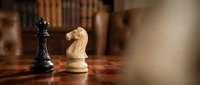 Chess pieces on wooden board with black king and white knight in strategic position for game planning and tactical thinking.
