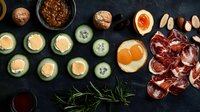 Fresh cucumber rolls with salmon, sliced prosciutto, soft boiled egg, nuts and spices on dark background. Appetizer platter for restaurant menu.