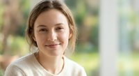 Young Caucasian woman with blonde hair smiling warmly at camera in casual beige sweater. Natural lighting creates soft portrait for lifestyle content.