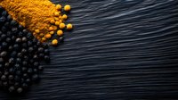 Fresh blueberries and turmeric powder spilled on dark wooden surface creating colorful contrast for healthy cooking and natural ingredients concept.