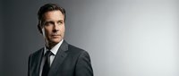 Professional businessman in elegant suit portrait with confident expression against gradient background for corporate marketing materials.