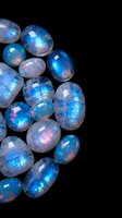 Luminous rainbow moonstone gems with iridescent blue fire scattered on black background for jewelry design and gemstone collection displays.