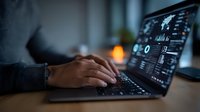 Hands typing on laptop keyboard with data analytics dashboard displayed on screen in dark office setting with ambient lighting and blurred background.
