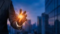 Businessman holding glowing energy orb with sparkling light effects against blurred city skyline at dusk, representing power, innovation, technology, and business success.