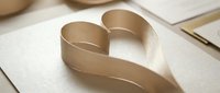 Elegant beige ribbon shaped into heart symbol on textured paper background for romantic greeting cards, wedding invitations and love-themed designs.