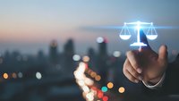 Hand touching glowing scales of justice icon over blurred city skyline at dusk for legal technology and law firm digital services.