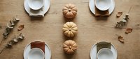 Autumn table setting with mini pumpkins and eucalyptus leaves on wooden background. Fall dining decor for Thanksgiving celebration and seasonal gatherings.
