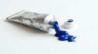 Squeezed paint tube with vibrant blue acrylic paint spilling out on clean white background. Art supplies for creative projects and artistic expression.