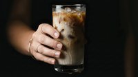 Cold cola drink with ice in glass held by hand against dark background, refreshing beverage for advertising and commercial use.