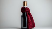 Dark wine bottle wrapped in cozy burgundy knitted scarf against neutral background, minimalist winter holiday concept for wine and spirits marketing.