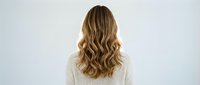 Woman with long wavy blonde hair wearing white knit sweater from behind on light background for hair care beauty salon advertising concepts.