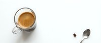 Overhead view of hot espresso coffee in glass cup with handle on white surface, minimalist flat lay composition for beverage and café design projects.