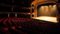 Classic theater interior with red velvet seats and ornate golden stage architecture under warm dramatic lighting for performing arts venues.