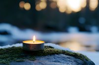 Peaceful candle flame glowing on moss-covered stone during winter evening creating warm ambient light for meditation and relaxation outdoors.