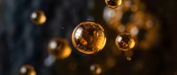 Golden oil bubbles floating in dark liquid creating abstract luxury cosmetic background with warm bokeh lighting effects.
