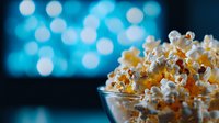 Fresh popcorn in glass bowl against blurred blue bokeh lights background, cinematic mood for movie night entertainment and snack concept.