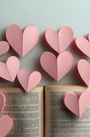Pink paper hearts floating above open book pages creating romantic literary concept for love stories and Valentine's Day celebrations.