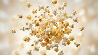 Fresh popcorn kernels exploding and flying through air against warm golden background. Perfect for snack food advertising and entertainment concepts.