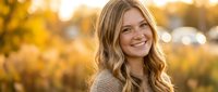 Young blonde woman smiling warmly in golden autumn sunlight with soft bokeh background, natural portrait photography for lifestyle and wellness content.