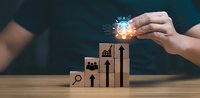 Business growth strategy concept with wooden blocks showing ascending arrows and icons while hand holds glowing light bulb representing innovation.