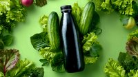Fresh green vegetables and black bottle on green background. Healthy detox drink concept with organic produce and lettuce leaves arranged in flat lay composition.