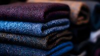 Stack of folded denim jeans in blue and purple shades showing detailed textile texture and fabric weave patterns in dark moody lighting for fashion retail.