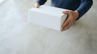 Man in dark clothing holding white cardboard box on concrete floor, overhead view for delivery, shipping, logistics, e-commerce, and packaging concepts.