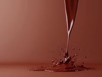 Liquid chocolate stream pouring and splashing on brown background creating dynamic splash effect with droplets and ripples. Appetizing food photography.