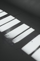 Dramatic light and shadow pattern from window blinds creating geometric stripes on dark floor, minimalist abstract architectural photography in black and white.