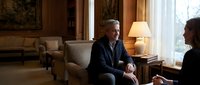 Mature man with gray hair and light skin tone, wearing dark blazer, seated in upscale living room during conversation. Suitable for business, lifestyle, corporate communications, and editorial use.