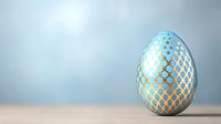 Decorative Easter egg in light blue and gold geometric pattern on soft blurred background. Modern festive spring holiday concept.
