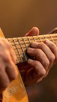 Close-up of male musician hands playing electric guitar with warm golden lighting creating atmospheric mood for music and performance concepts.