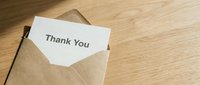 Thank you card peeking out of a kraft paper envelope on a wooden surface, conveying gratitude and appreciation in a warm, minimal style.