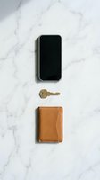 Modern smartphone with leather wallet and house key arranged on white marble surface for everyday carry essentials and minimalist lifestyle concepts.