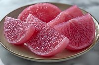 Fresh pink grapefruit segments on ceramic plate showing juicy pulp texture and natural citrus flesh detail in macro photography for food styling.