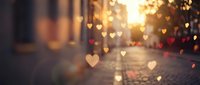 Blurred city street at golden sunset with glowing heart-shaped bokeh lights, romantic Valentine's Day atmosphere for greeting cards and backgrounds.