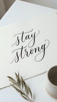 Stay strong handwritten calligraphy on white paper with dried botanical elements and coffee cup, motivational quote for greeting cards, wall art, and inspirational designs.