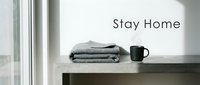 Cozy stay home concept with folded gray knit blanket and black mug on concrete shelf near bright window, minimal interior lifestyle.