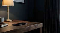 Modern workspace with wooden desk, glowing table lamp, smartphone, and dark curtains in minimalist office setting.