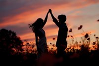 Silhouette of couple holding hands up in celebration against vibrant sunset sky with wildflowers for romantic relationship and love concepts.