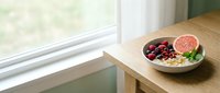 Healthy breakfast bowl with granola, berries, grapefruit and yogurt on wooden table by window, perfect for food and wellness content.