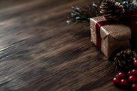 Festive gift box wrapped in gold paper with red ribbon, pine cones and red berries on rustic wooden background with copy space for holiday designs.
