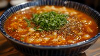 Spicy ramen noodle soup with chili oil, garnished with green onions in ceramic bowl, Asian cuisine comfort food.