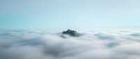 Mountain peak emerging from thick cloud cover at dawn, surrounded by sea of white mist and fog, suitable for nature, travel, and inspirational design projects.