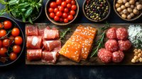 Fresh raw salmon fillet, prosciutto rolls, meatballs with herbs, cherry tomatoes, and assorted spices on dark wooden board, top view food composition.